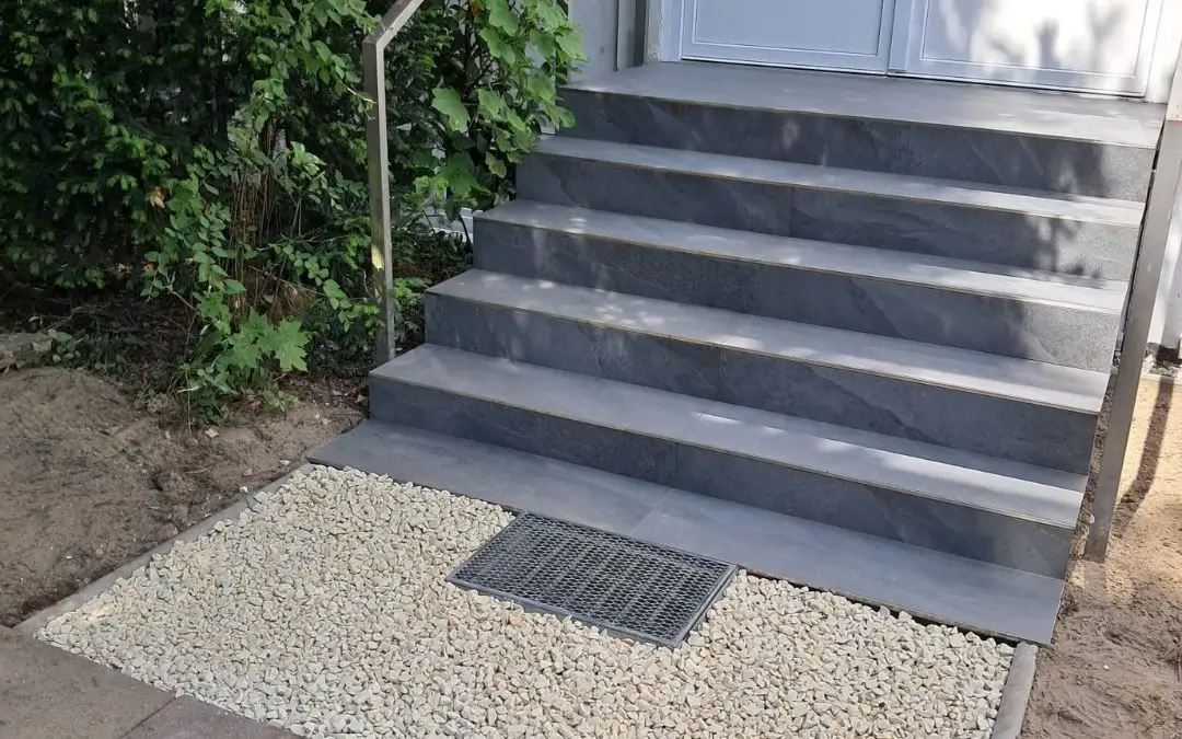 Die Treppe zum Gemeinderaum ist erneuert. Die Stufen in einem dunklen grau. Davor heller Kies.
