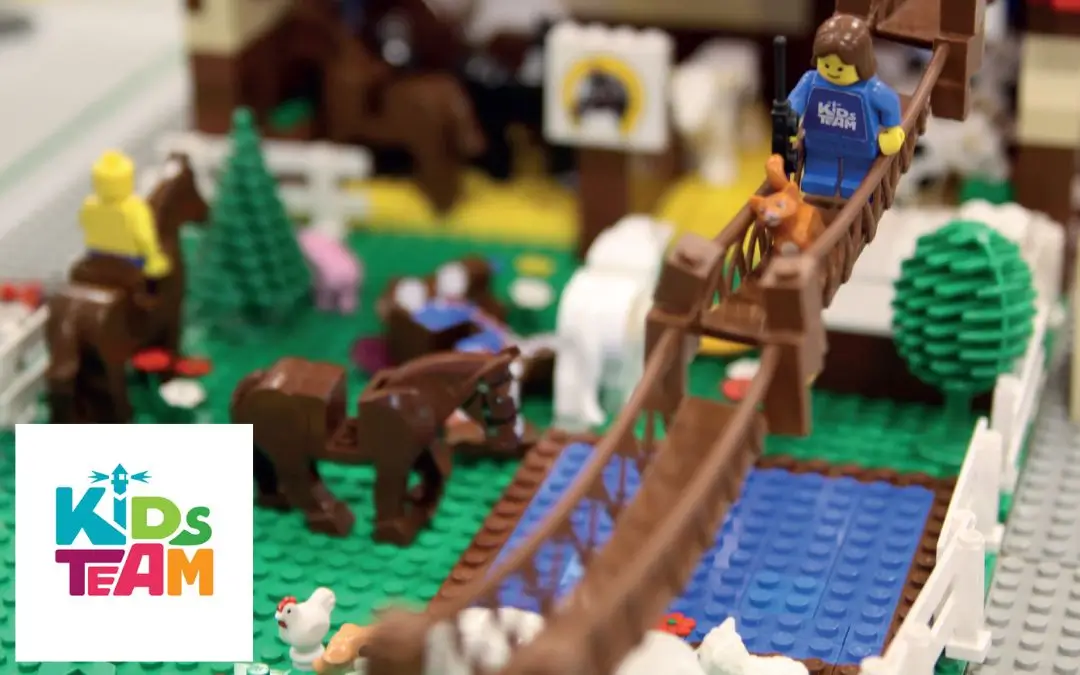 Eine kreative Lego-Landschaft mit Tieren, Hängebrücke und einem Stall. In der Ecke das Logo vom Veranstalter Kids Team.