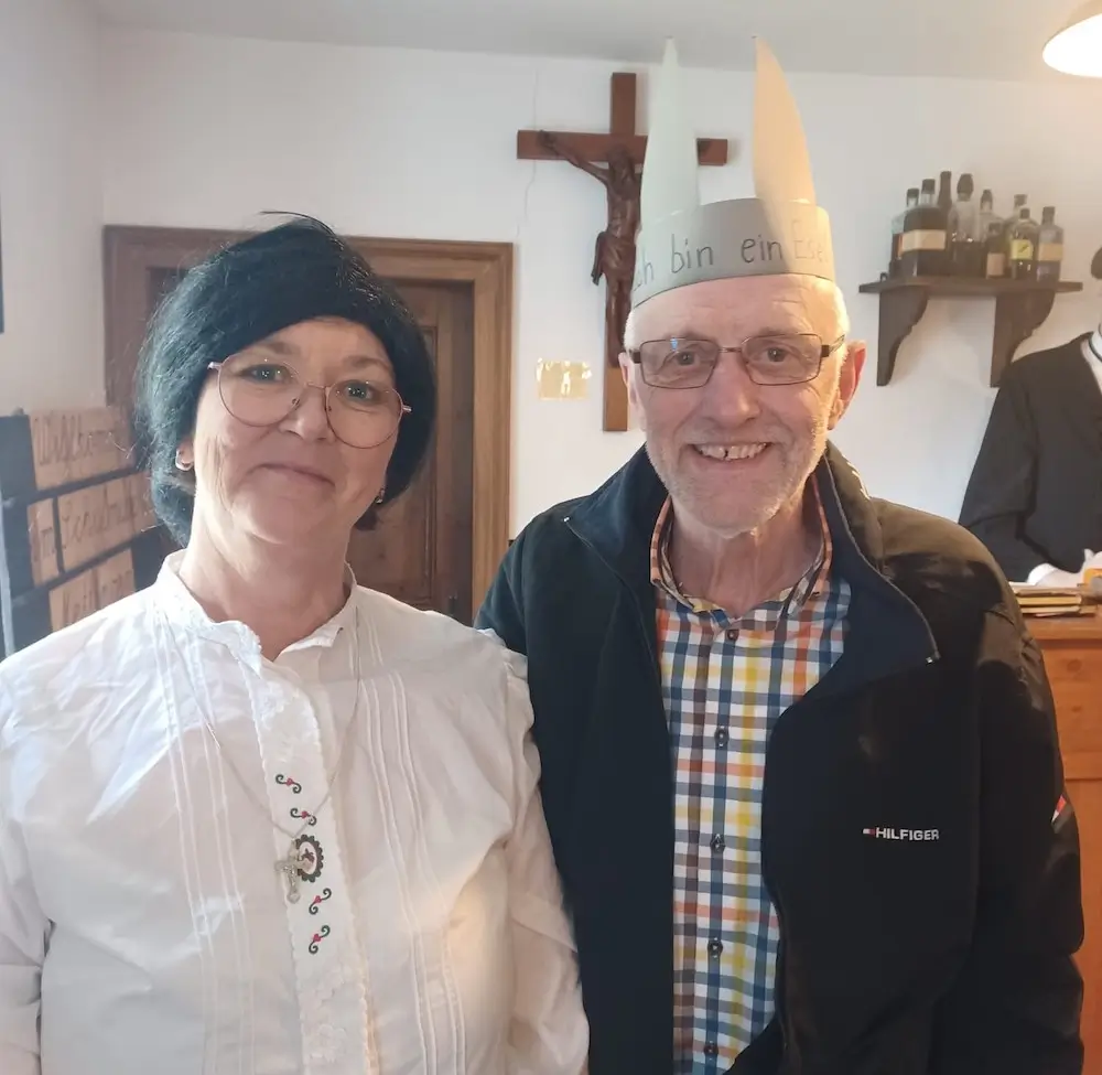 Eine Lehrerin vom "Damals" mit einem Herren, der eine Krone mit Ohren trägt, auf der "Ich bin ein Esel" steht.