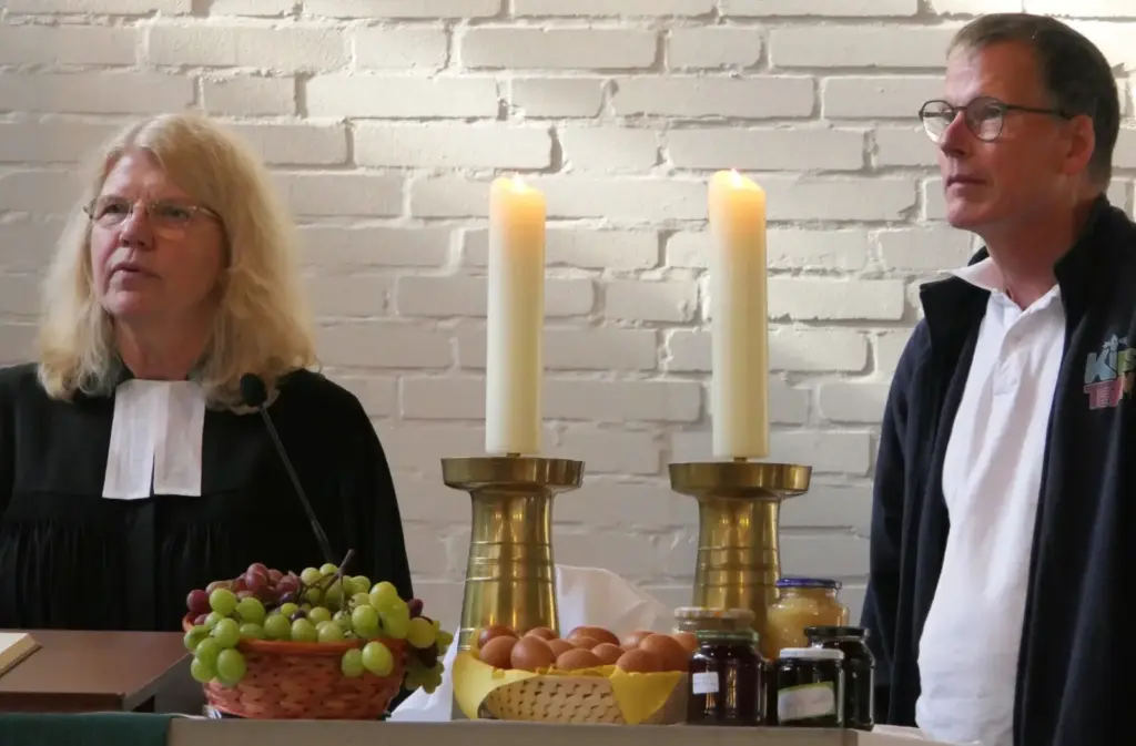 Pfarrerin Holtgrave und Knut Ahlborn hinter dem Altar mit Erntegaben und brennenden Kerzen zum Erntedankgottesdienst in der Johanneskirche