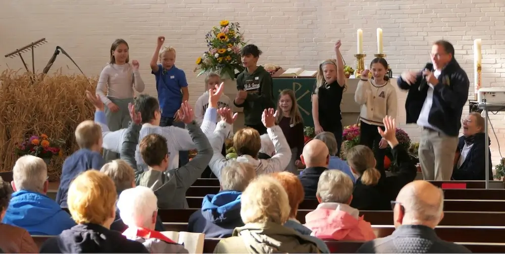 Die Kinder vom Lego Projekt singen mit Knut Ahlborn ein Lied vor dem Altar in der Johanneskirche. Die Gemeinde macht die Bewegungen zum Lied mit.